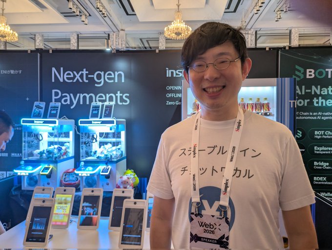 A smiling man wearing glasses and a Web×2026 speaker t-shirt with Japanese text ("シンプルなイン, チャット, カル") stands at the INSPAY booth promoting their "Next-gen Payments" vending machine system, which features multiple payment terminals and displays reading "AI-Native" technology for autonomous AI agents.