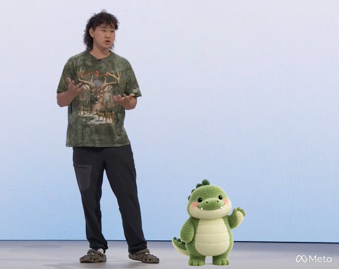 A man wearing a deer graphic t-shirt stands on stage next to a green plush dinosaur mascot, with a Meta logo in the corner.