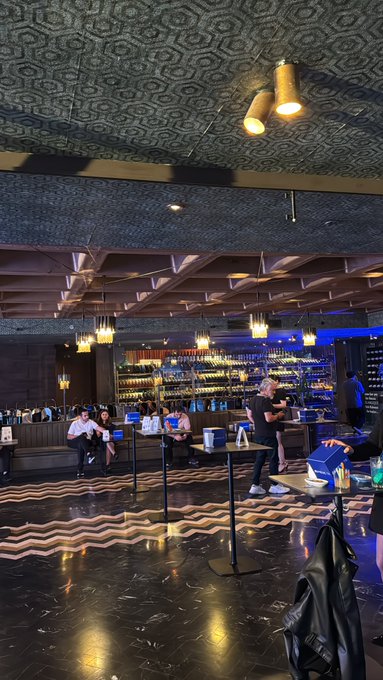The image shows a large room with black and white checkered floors, featuring several people sitting at tables or standing around. The room has a high ceiling with decorative elements such as lights and a chandelier hanging from the center of the ceiling. There are also some bottles placed on surfaces in the room. The post accompanying this image is titled "Istanbul’daki @Mexctrcom VIP gecesinde gizli üç ödülün peşindeyim Keskin gözler." which translates to "Istanbul's best" and "VIP gecesinde gizli üçÖdün peşindeyim Keskin gözler". The post is about a special event happening in Istanbul, Turkey.