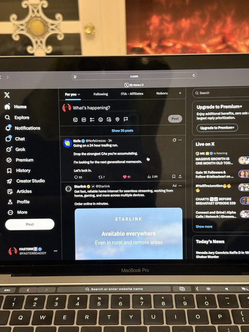 A MacBook Pro displaying the X (Twitter) social media platform with a post about Starlink being available everywhere, shown in front of a fireplace.