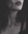 A dark, moody portrait of a woman with dark lipstick and messy hair, with only the lower half of her face clearly visible against a shadowy background.