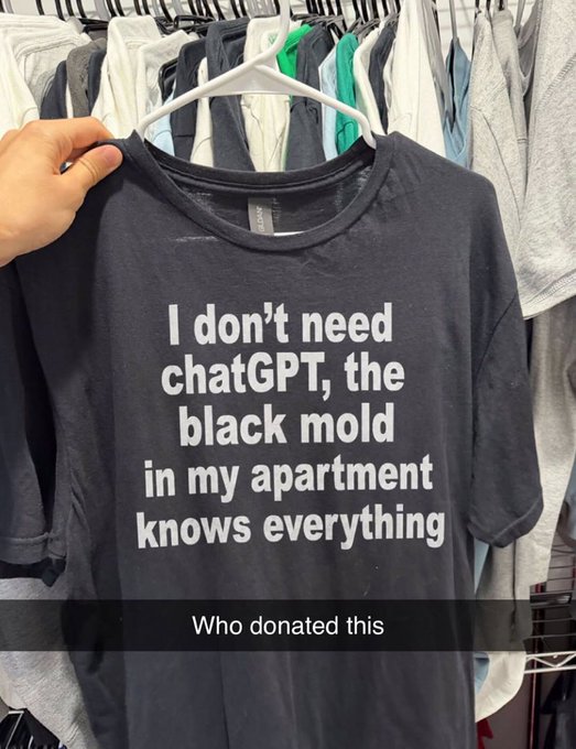 A person holds up a black t-shirt on a hanger that reads 'I don't need chatGPT, the black mold in my apartment knows everything,' with a caption below asking 'Who donated this.'