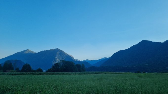 The image depicts a serene landscape with a green field under a clear blue sky, framed by rugged mountains. The "GM legends" caption suggests a focus on General Motors' iconic vehicles or influential figures associated with the brand, perhaps symbolizing the timeless and enduring qualities of these legends, akin to the classic beauty of the natural scene presented.