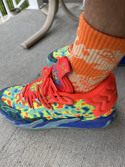Photo of colorful, vibrant graffiti-patterned Nike basketball sneakers worn with orange patterned socks on a patio.