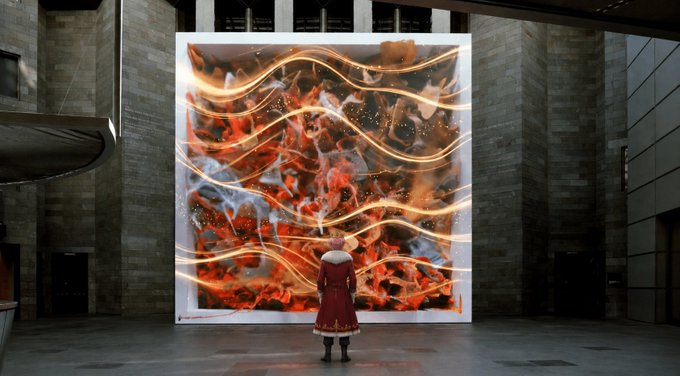 The image features a person wearing a red coat standing in front of an art piece, which appears to be a large painting or sculpture with orange and white colors. The person seems to be looking at the artwork closely, possibly admiring its details or contemplating its meaning. The focus on this individual and their interaction with the art piece highlights the importance of human engagement and appreciation for artistic expression in today's technology-driven world.
