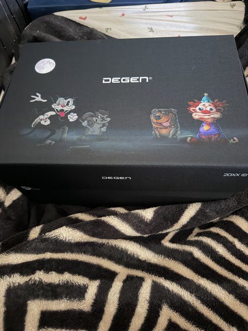 A black DEGEN-branded mystery box featuring cartoon characters (a ghost, a tiger, a dog, and a clown) sitting on a zebra-print blanket.