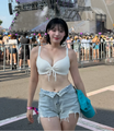 An image of a woman in a white bikini top and light-colored shorts walking in a crowded public area.