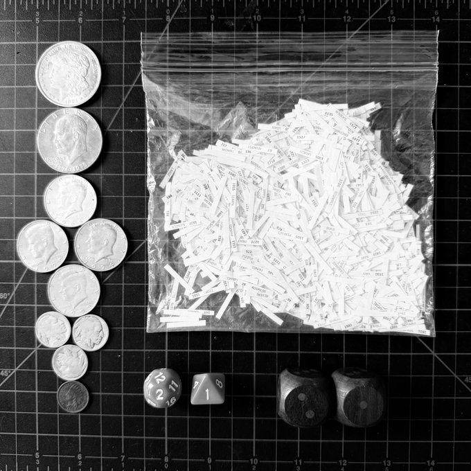 A black-and-white photo displays various coins (including what appear to be Eisenhower, Kennedy, Roosevelt, and Buffalo nickels, plus a Mercury dime) arranged alongside a clear plastic bag filled with paper slips labeled "front" and "back," two dice, and two large dice, all resting on a gridded cutting mat. The collection visually represents "rolling your own entropy"—using physical randomness from dice and paper chits alongside precious metal coinage—to generate true random numbers for securing cryptocurrency seed phrases or other sensitive data, ensuring the owner's "sovereign stack" can be passed down through generations.