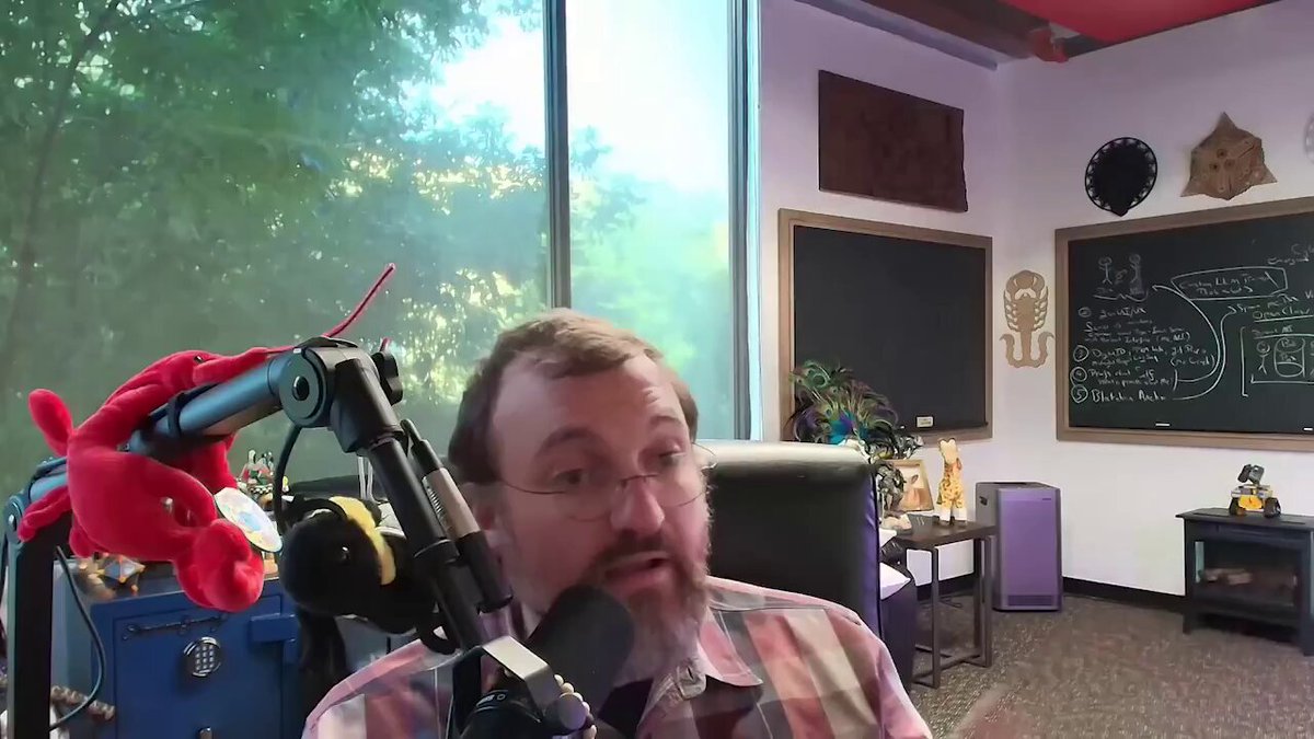 The image shows a man wearing glasses sitting behind a microphone, likely participating in a podcast or radio show. The background features a window with trees outside, suggesting an outdoor setting for the event. The caption of the image reads "@Cardano is going to completely overtake Bitcoin and the rest of the market is simply not ready for it! When we say that this ecosystem will surprise everyone we are speaking the absolute truth". This statement seems to be related to the ongoing discussion about the potential impact of Cardano on the cryptocurrency market.
