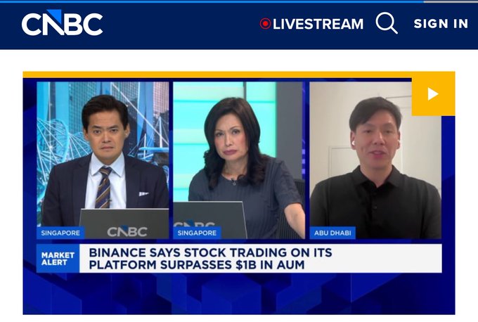 A CNBC livestream screenshot featuring two anchors in Singapore and a guest in Abu Dhabi, with a market alert reading 'BINANCE SAYS STOCK TRADING ON ITS PLATFORM SURPASSES $1B IN AUM'.