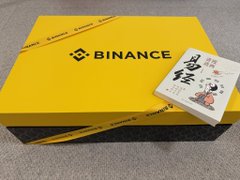 The image features a large yellow box with "Binance" written on it, along with a book placed next to it. The box appears to contain a giant Dragon Boat Festival-themed gift, possibly related to tennis or sports equipment. The book is open, revealing its contents inside. The post includes an image of the gift box and the book, as well as text that reads "Today I received a giant Dragon Boat Festival giveaway from Binance @ binancezh It's truly an enormous gift box. Opened it up and there was a surprise inside—it turned out to be a tennis kit, super awesome."