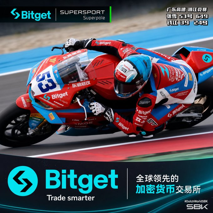 The image features a person riding a motorcycle, wearing a racing suit with blue and red colors. The motorcycle has a number of sponsors on its body, including Bitget. The scene takes place on a race track or a similar setting where the rider is actively participating in a motorbike race.