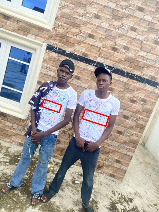 Photo of two young men standing outdoors in front of a brick building, wearing white t-shirts with handwritten messages and red box markings highlighting words like 'INSET' and 'UNSELF'.