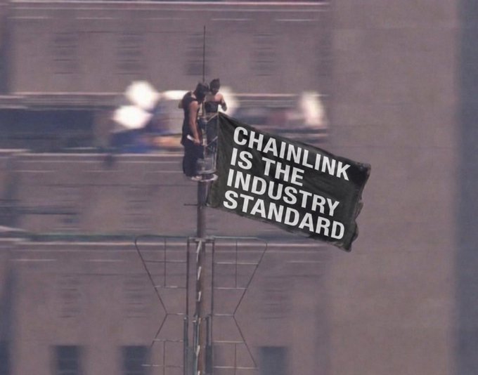 A grainy photo of two people on top of a tall structure holding a black banner that reads 'CHAINLINK IS THE INDUSTRY STANDARD'.