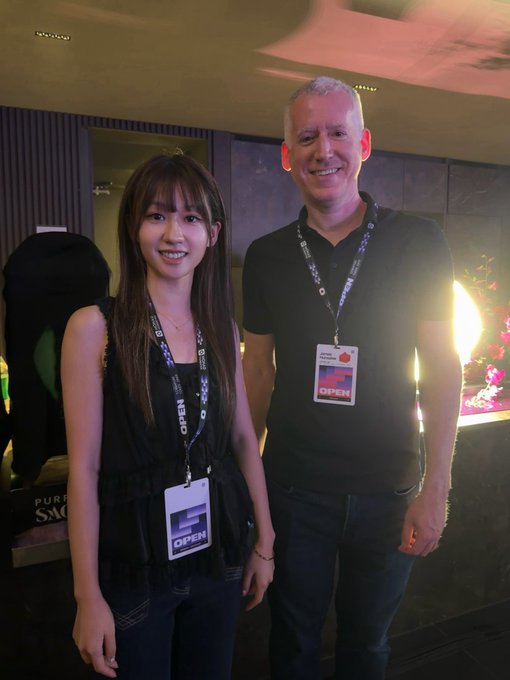 A young woman and an older man smile for a photo, both wearing 'OPEN' lanyard badges around their necks.