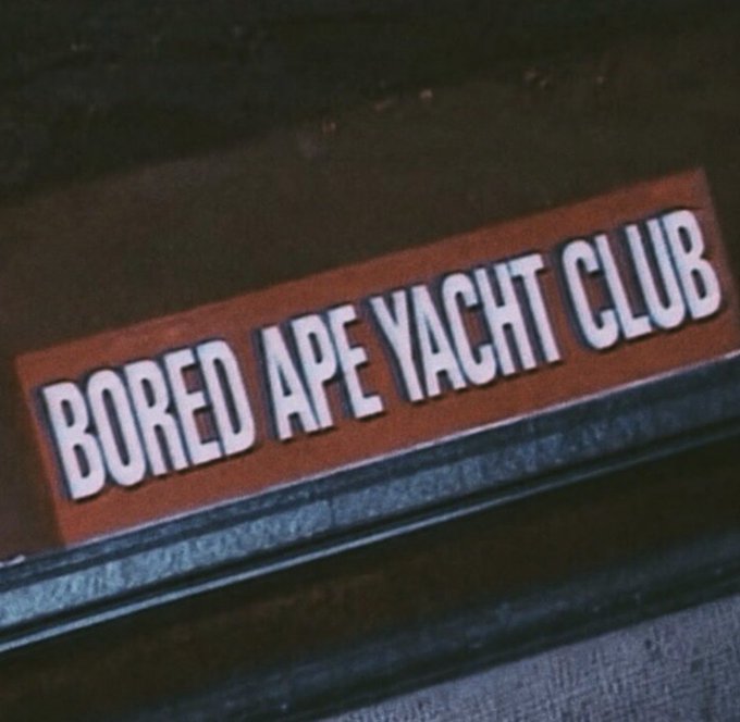 A sticker with the text "BORED APE YACHT CLUB" in white block letters on an orange background, affixed to a dark surface, directly illustrating the NFT brand name referenced in the post.