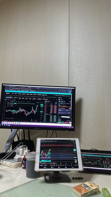A trading setup featuring a monitor displaying cryptocurrency charts, a tablet showing similar charts, and another screen with market data on a desk.