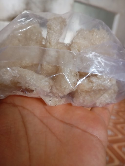 A hand holds up a clear plastic bag containing several pieces of sugared/snowy white food items, possibly candied ginger or a similar snack.