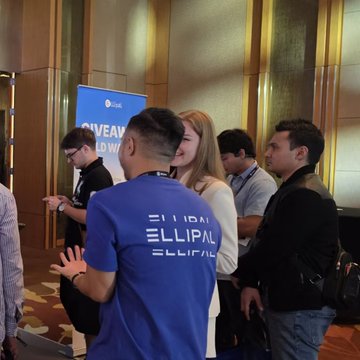 A group gathers around the ELLIPAL booth at TOKEN2049 Singapore, where a staff member in a branded blue shirt engages with attendees near a "WEB3" display at Marina Bay Sands.