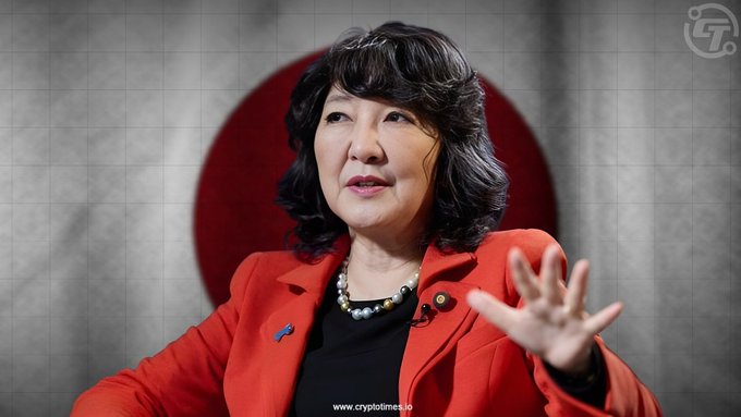 The image shows a woman with dark hair wearing a red blazer and pearl necklace, gesturing with her hand, set against a backdrop featuring the Japanese flag. The watermark reads "www.cryptotimes.io," suggesting the photo is tied to coverage of Japan's comprehensive new cryptocurrency legislation mentioned in the post.