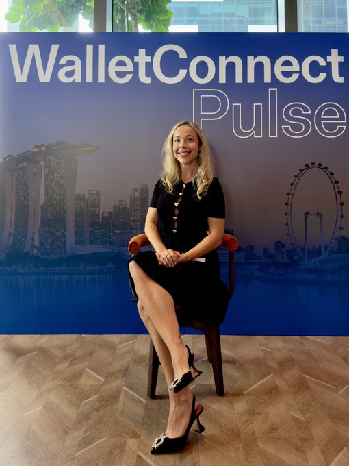 A woman in a black dress and high heels sits on a chair smiling in front of a 'WalletConnect Pulse' banner featuring a Singapore skyline.