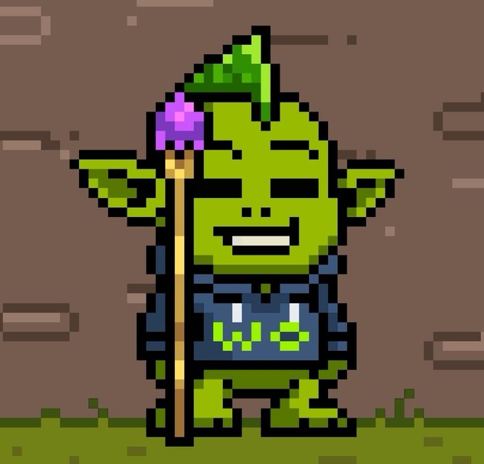Pixel art of a green goblin-like character wearing a leaf hat, grinning while holding a staff with a purple crystal, set against a brown brick wall background.