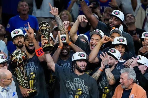 The Oklahoma City Thunder basketball team celebrates with the NBA Championship trophy while wearing 'NBA Champions' t-shirts and hats.