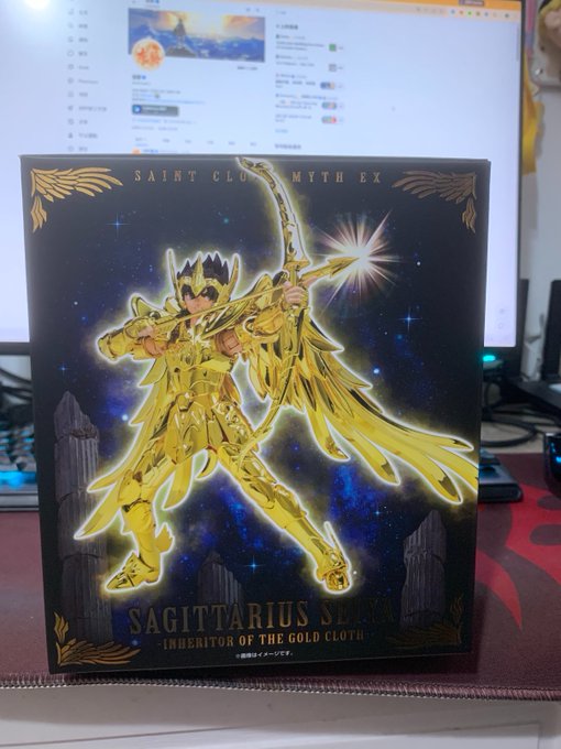 A box for the 'Saint Cloth Myth EX Sagittarius Seiya - Inheritor of the Gold Cloth' figure sits in front of a computer monitor.