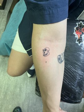 A photo showing a person's leg with two small cartoon-style temporary tattoos or henna designs of robot/character faces, taken from a first-person perspective.
