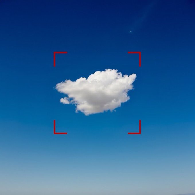 A single white cloud centered in a clear blue sky, framed by red camera focus brackets.
