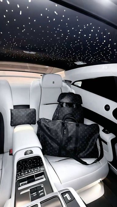 The luxurious white interior of a Rolls-Royce car, featuring a starlight headliner ceiling and custom Louis Vuitton monogram luggage placed on the passenger seat.