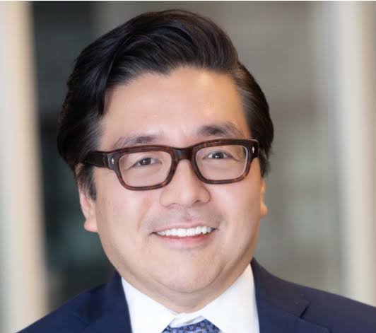A professional headshot of an Asian man wearing glasses and a navy blue suit, smiling at the camera.