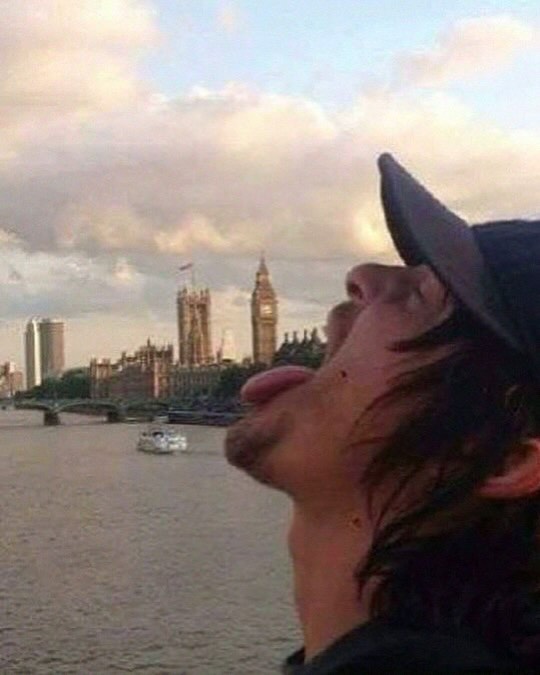 A person wearing a Batman mask making a face with their tongue out, with the Palace of Westminster and the River Thames visible in the background.