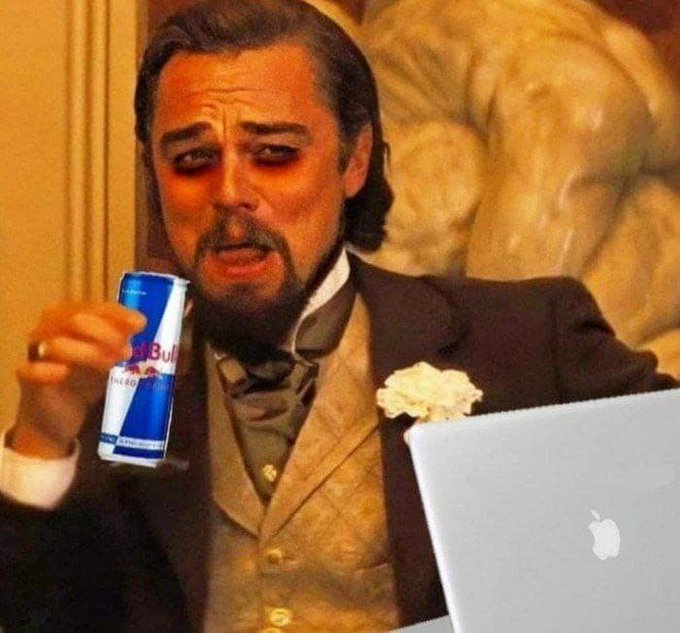The image features a man dressed in a suit, holding a can of Red Bull while sitting at a desk with an Apple laptop open in front of him. The caption reads "tell that to Levy", which could be interpreted as a reference to the character Leonard Levy from the movie "The Godfather".