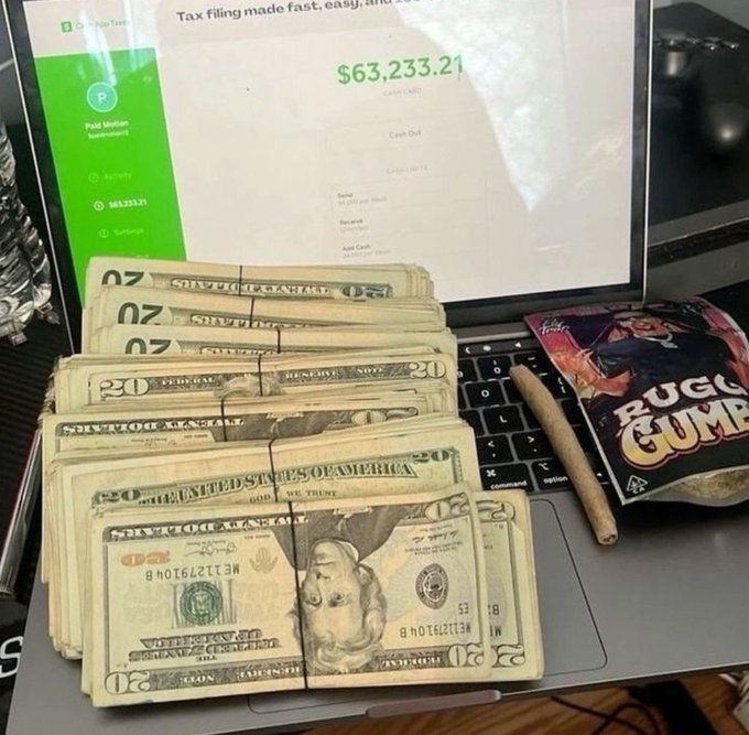 A pile of cash sits on a laptop displaying a Paid Motion account with a balance of $63,233.21, perfectly aligning with the post's theme of "grinding for the money."