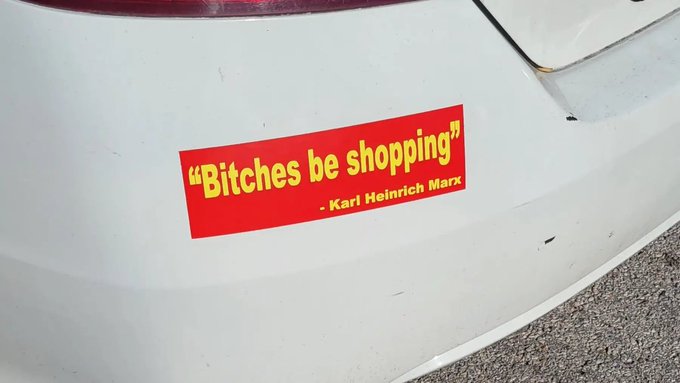 A red bumper sticker on a white car reads 'Bitches be shopping' attributed to Karl Heinrich Marx.