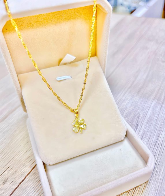 A gold chain necklace with a four-leaf clover pendant resting inside a cream-colored velvet jewelry box.