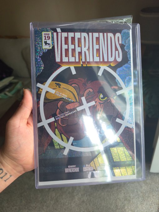 A hand holding a slabbed 'VEEFRIENDS' graded comic book (grade 9) with a ransom-note style logo and colorful character artwork featuring creators Gary Vaynerchuk, DJ Coffman, and others.