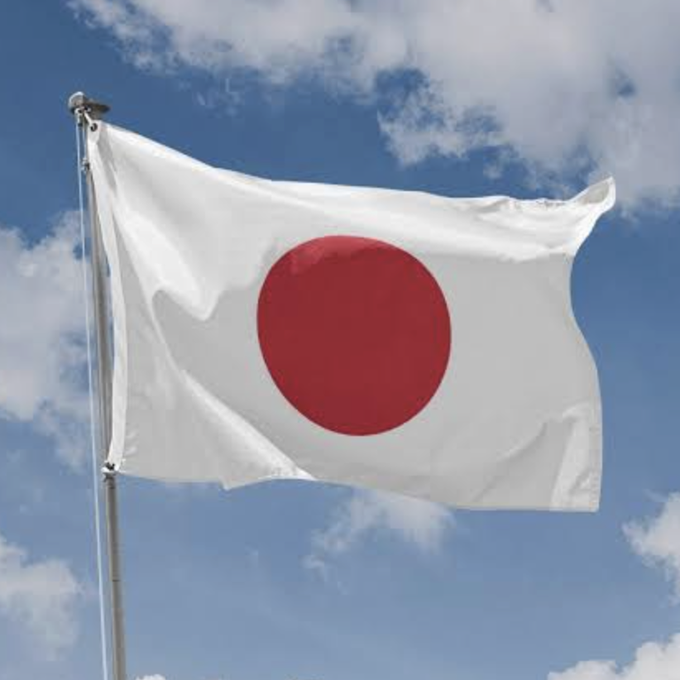 The Japanese flag waves against a blue sky, representing Japan's initiative to develop a blockchain-based stock and government bond settlement system by early 2027.