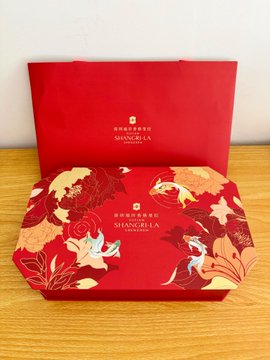 Two red Shangri-La mooncake gift boxes with gold floral and bird designs sitting on a wooden surface.