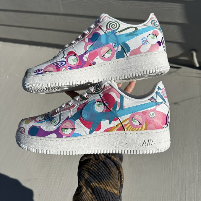 Pair of Nike Air Force 1 sneakers featuring colorful pastel custom artwork with eyes, swirls, and abstract patterns held up outdoors.