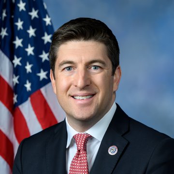 A man in a dark suit and red patterned tie smiles in an official portrait, with an American flag displayed behind him and a lapel pin visible on his jacket.

The image appears to be an official congressional portrait that relates to the post's mention of the "Clarity Act," as the legislation concerns a U.S. congressman whose vote is being referenced regarding cryptocurrency policy decisions expected around September 15th.