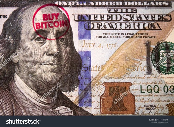 A close-up of a US $100 bill featuring Benjamin Franklin with a red stamp reading 'BUY BITCOIN' on his forehead.