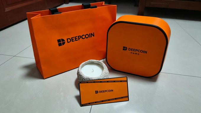 A collection of orange DeepCoin branded merchandise, including a paper shopping bag, a zippered case, and a card, displayed on a tiled floor next to a candle.