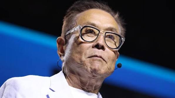An older man with short gray hair and thick black-rimmed glasses looks upward thoughtfully while wearing a headset microphone against a blue-lit stage background. The image accompanies the post about Robert Kiyosaki predicting that Ethereum ($ETH) could reach $95,000 by mid-2027.