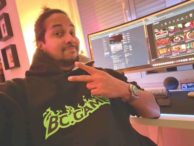 A man wearing a black "Buddah" hoodie with green logo throws up a peace sign while sitting in front of dual monitors displaying streaming/recording software, with the post's "Gn CT" caption suggesting a goodnight message from Connecticut to his audience.
