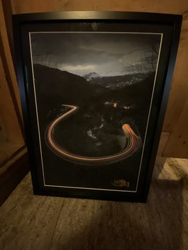 A framed, museum-grade artwork of a mountainous landscape with a glowing U-shaped light trail rests in a custom black frame, as referenced in the post about two signed pieces ("0xFlow alpha" and "0xFlow delta," including a 1/1 commission) being ready for delivery to their new home.