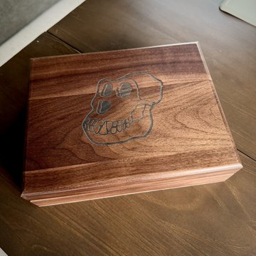 A wooden box with a carved or engraved skull design on its lid, sitting on a wooden surface.