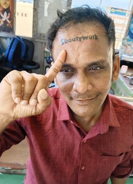 The image features a man with a tattoo of "shoutwork" written above his eye. He is wearing a red shirt and pointing at the tattoo while making a funny face for the camera, possibly as part of a joke or playful gesture. The caption in the image reads: "Finally, the shameful narrative is gone." This suggests that the man's tattoo has been removed or altered to remove any negative connotations associated with it.