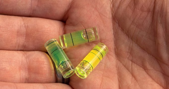 Close-up photograph of a hand holding three small, transparent yellow-green cylindrical vials, each containing a bubble level indicator common to fishing equipment.